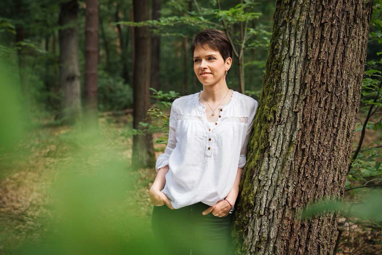 Frau steht im Wald lehnend an einem Baum